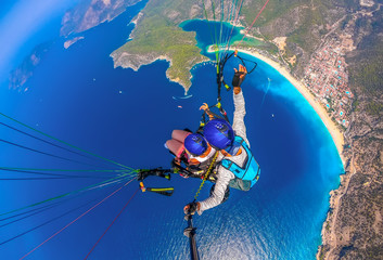 Paragliding in the sky. Paraglider tandem flying over the sea with blue water and mountains in...