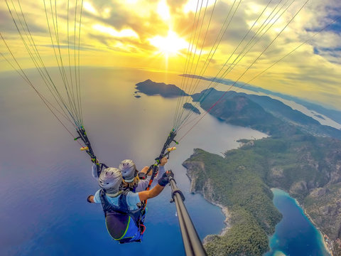 Paragliding in the sky. Paraglider tandem flying over the sea with blue water and mountains in bright sunny day. Aerial view of paraglider and Blue Lagoon in Oludeniz, Turkey.