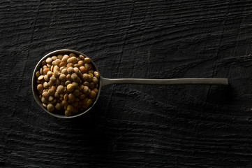 Raw, dry, uncooked brown lentil legumes in metal scoop on wood table background top view flat lay...