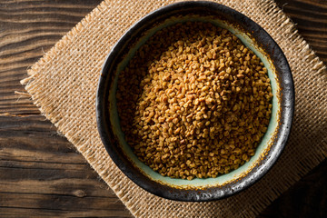 Dried, raw fenugreek seed in bowl on rustic wooden table background top view flat lay from above