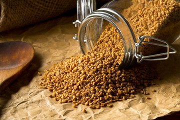 Dried, raw fenugreek seed in storage glass jar on brown packing paper background