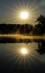 Sunrise mirrored on calm lake waters with fog on the water
