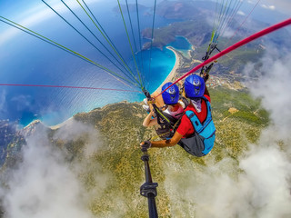 Paragliding in the sky. Paraglider tandem flying over the sea with blue water and mountains in bright sunny day. Aerial view of paraglider and Blue Lagoon in Oludeniz, Turkey.
