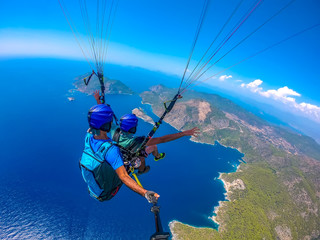 Paragliding in the sky. Paraglider tandem flying over the sea with blue water and mountains in...