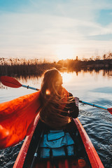 Back view of happy cute girl holding paddle in a kayak on the river