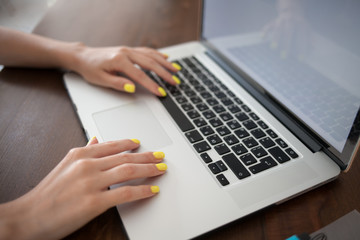Women's hands with trend yellow manicure typing text on a laptop keyboard.