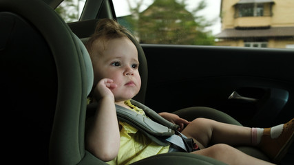 toddler girl yawns in dark green child car safety seat