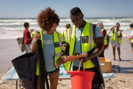 Volunteer couple discussing over clipboard at beach