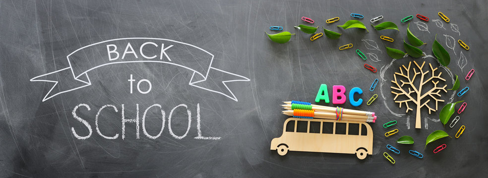 education and back to school concept. Top view photo of wooden bus and ABC letters, pencils on the roof next to tree with autumn leaves over classroom blackboard background. top view, flat lay
