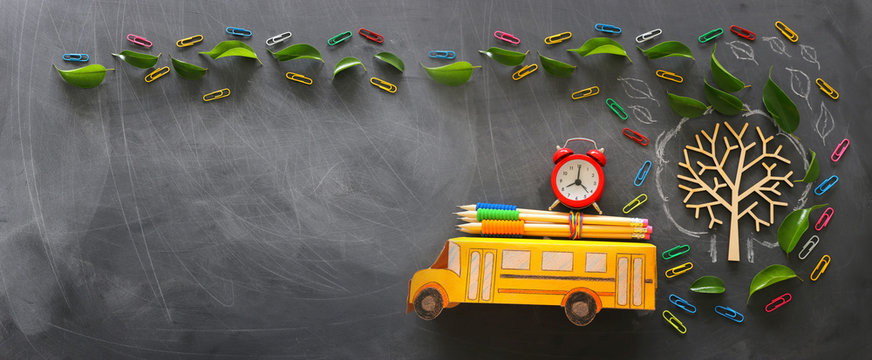 education and back to school concept. Top view photo of school bus and pencils, alarm clock on the roof next to tree with autumn leaves over classroom blackboard background. top view, flat lay