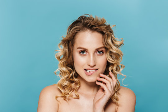 Beauty image of alluring half-naked woman with curly hair biting her lips and looking at camera