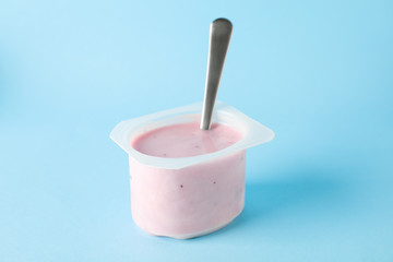 Plastic cup with yogurt and spoon on color background, space for text