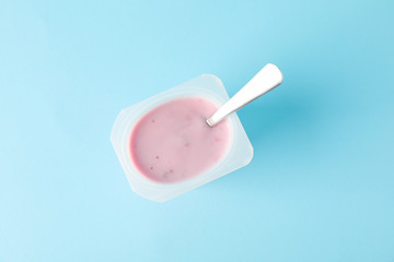 Plastic cup with yogurt and spoon on color background, space for text