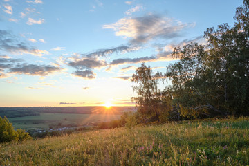 Naklejka na ściany i meble Beautiful sunset on a hill among the trees overlooking the village
