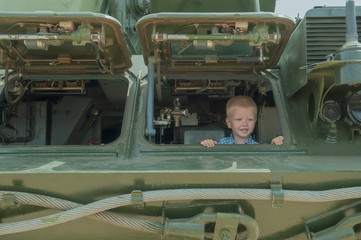 blond child in plaid shirt plays in old military vehicle. kid looks out of viewing hatch. concept of contrasting innocent childhood and war