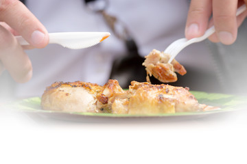 person eating chicken shish kebab on plate by using plastic fork and knife side closeup view of grilled meat and sauce on white copy space background street food in outdoor authentic lifestyle concept