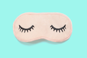Pastel pink sleep mask with closed eyes embroidered on it with eyelashes on turquoise background. Top view, flat lay. Concept of vivid dreams. Accessories for girls and young women. Minimal style