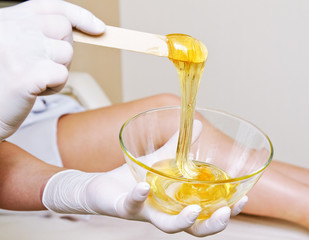 Cosmetologist master holding bowl with hot wax for depilation epilation hair removal procedure and...
