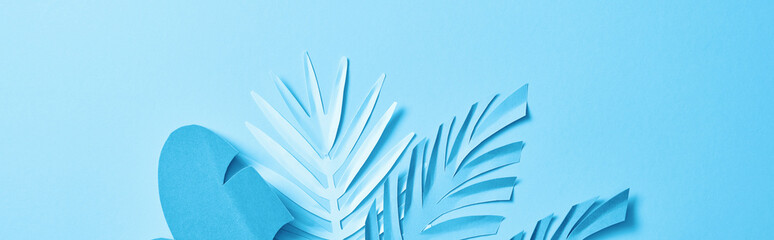 top view of blue exotic paper cut palm leaves on blue background with copy space, panoramic shot
