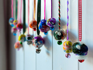 Homemade Christmas baubles hanging in a row. Made from colourful felted wool with ribbons and bells. Back lit with selective focus on white wooden background.