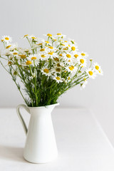 Daisy chamomile bouquet in vase on white table. Side view with copy space. Country style