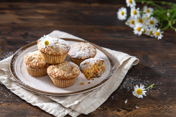 Carrot cake muffins with nuts, raisins and oats on a dark background. Carrot and daisies bouquet on the table. Country style. Copy space