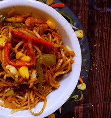 Veg noodles in a bowl topped with capsicum,sweet corn and herbs