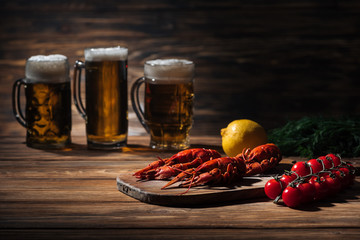 selective focus of red lobsters, tomatoes, dill, lemon and glasses with beer on wooden surface