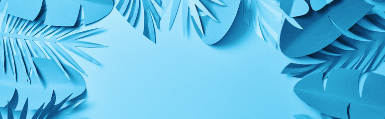 top view of blue minimalistic paper cut palm leaves on blue background with copy space, panoramic shot