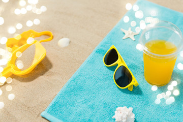 vacation, travel and summer holidays concept - yellow sunglasses, sand toys, seashells and juice drink on beach towel