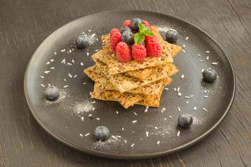 Biscuits with whole grains. Raspberry and blueberry berries on top. Black plate, top view