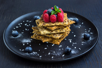 Cookies with whole grains. Raspberry and blueberry berries with icing sugar on top. Black plate, black background.