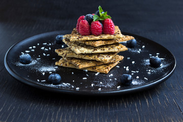 Cookies with whole grains. Raspberry and blueberry berries with icing sugar on top. Black plate, black background.