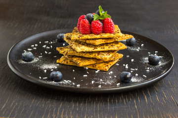 Cookies with whole grains. Raspberry and blueberry berries with icing sugar on top. Black plate, black background.
