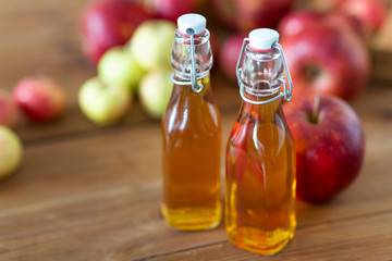 fruit drinks and season concept - glass bottles of apple juice, cider or vinegar on wooden table