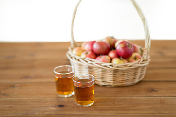 fruits, food and harvest concept - apples in wicker basket and glasses of juice on wooden table