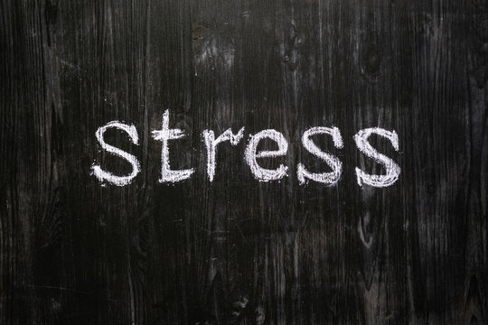 Stress word handwritten on black wood background. Sign, concept of mental issues - the word "stress" written with chalk on real blackboard
