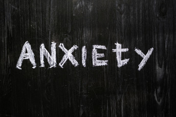 Anxiety word handwritten on black wood background. Sign, concept of mental issues - the word "anxiety" written with chalk on real blackboard