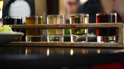 Multicolored transparent cocktails, a set of shots in one row, six servings on a wooden stand, substrate. Drink for the menu restaurant, bar, cafe