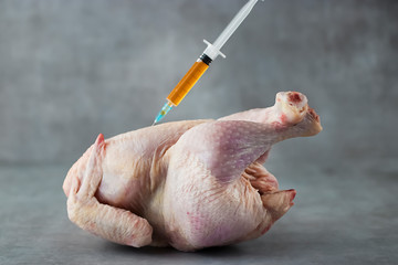 A chicken carcass and a syringe with antibiotic on a gray background.