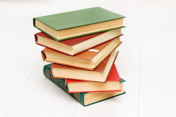 Stack of books is lying on a white wooden table. Green, red and brown covers.