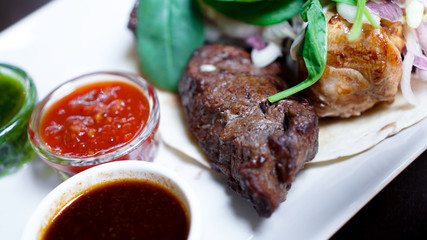 Pieces of meat with onions on skewers kebab. Serve with sauce on a white plate.