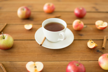 Obraz na płótnie Canvas objects and drinks concept - cup of black tea with apples and cinnamon on wooden table
