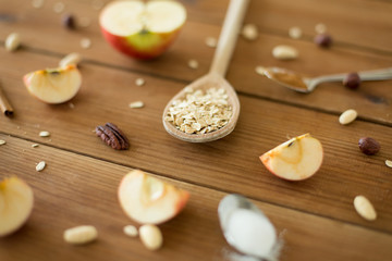Fototapeta na wymiar food cooking and eating concept - oatmeal in spoon, cut apples and nuts on wooden table