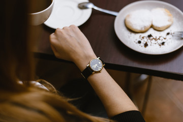 girl looks at the clock in a cafe over a cup of coffee. time on the clock - the time for breakfast, dessert