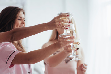 Close up view. Celebrating bachelorette in white bedroom. Girls smiles and drink champagne