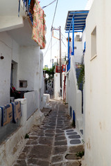Fototapeta na wymiar One of the charms of Mykonos, Greek island in the heart of the cyclades, are its narrow streets : white houses with small flowered balconies touching almost above paved streets