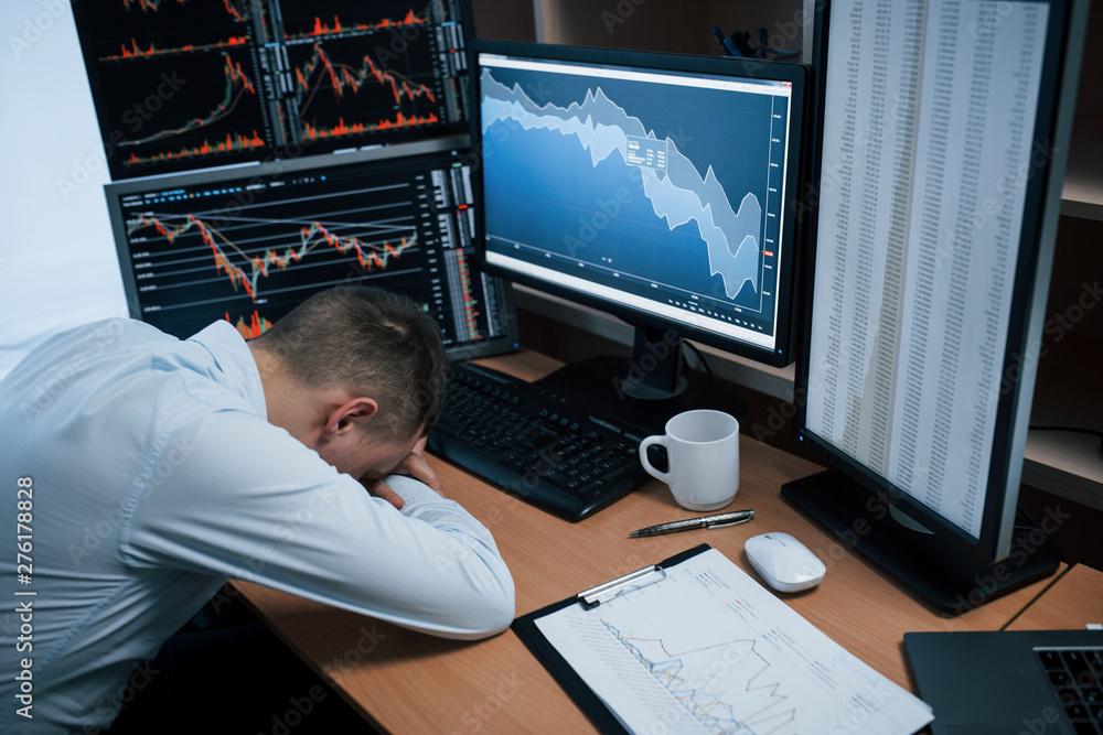 Poster tired of hard day. man working online in the office with multiple computer screens in index charts