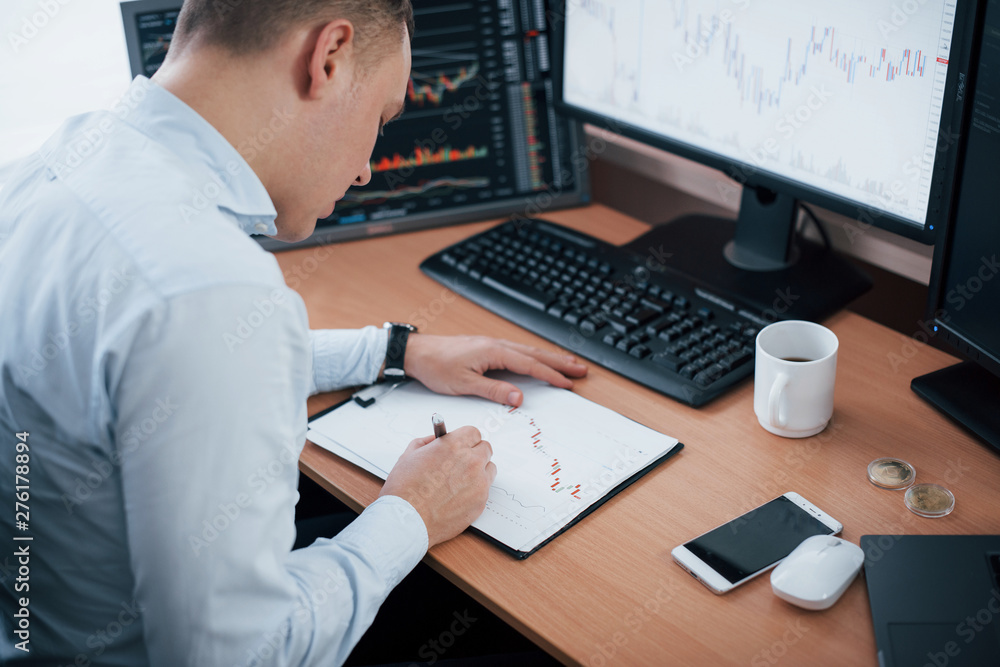 Poster corrections on the graphs on paper. man working online in the office with multiple computer screens 