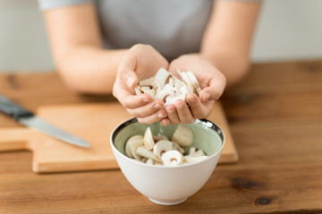 cooking, culinary and edible mushrooms concept - close up of woman holding chopped champignons